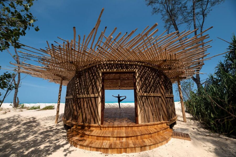 Una persona hace una postura de yoga en una cabaña frente al agua en las costas de Zanzíbar