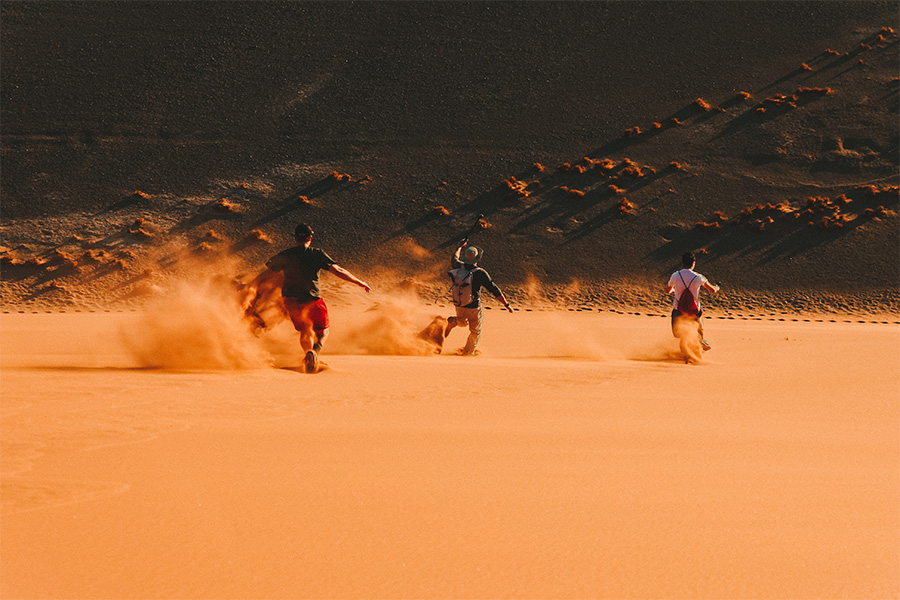 Three men running down a sand dune in Namibia.