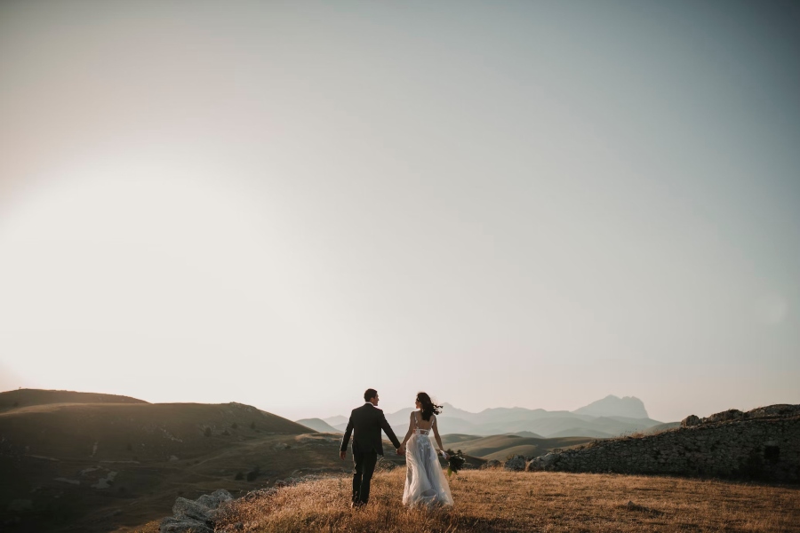 A couple who just got married holding hands heading away from the camera with a wide open space and mountains in the distance | Go2Africa