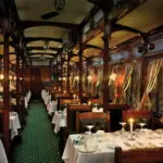 La vajilla de plata pulida refleja la luz de las velas en el vagón restaurante; se requiere vestimenta formal para la cena.