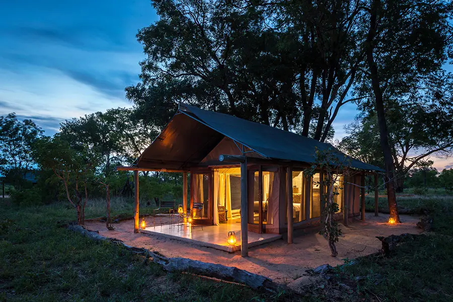 Una estructura de tiendas de campaña iluminada con linternas y luz desde el interior contrasta con la última luz del día y los oscuros árboles que hay detrás | Go2Africa