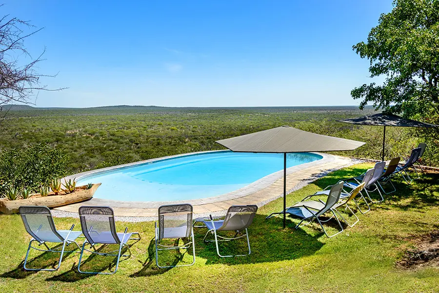 A bright blue pool with pool loungers and umbrellas facing away from the camera towards the view | Go2Africa