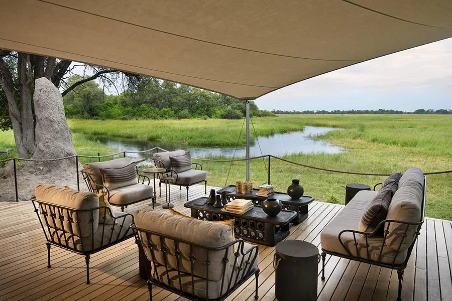 Una terraza de madera con una zona para sentarse y una mesa de café con vistas al agua y a la exuberante vegetación | Go2Africa