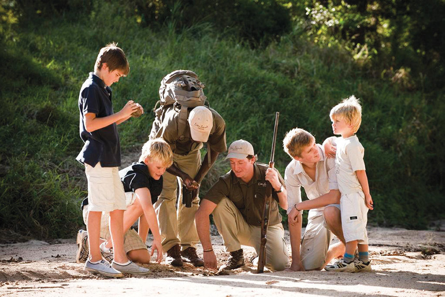 Several children gather around two guides from Lion Sands Lodge and look at tracks on the ground | Go2Africa