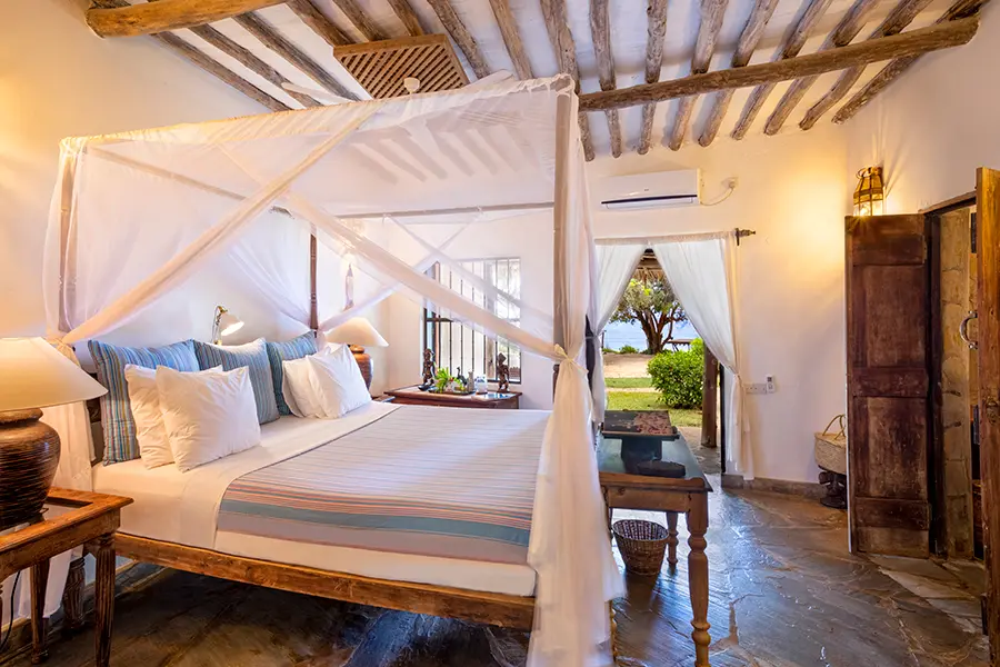 A white bedroom with elevated beach decor and a four-poster bed looks out to the beach and beyond to the ocean | Go2Africa