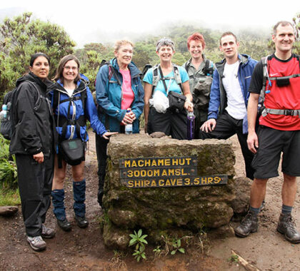 A happy-looking hiking group stands at the Machame Hut sign, looking forward to the next stage of the ascent.