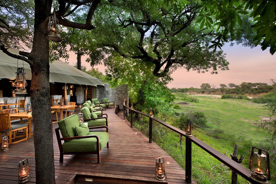 Several comfortable green armchairs with wooden arms and legs sit on a deck at Ngala Tented Camp overlooking the bush | Go2Africa