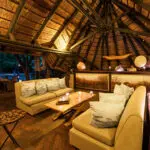 The lodge's main lounge & bar sit under thatch, flowing onto an outdoor deck with waterhole views.
