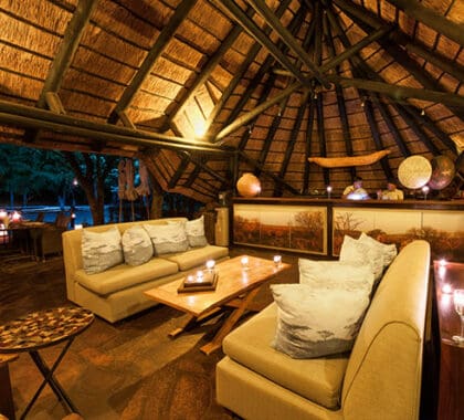 The lodge's main lounge & bar sit under thatch, flowing onto an outdoor deck with waterhole views.
