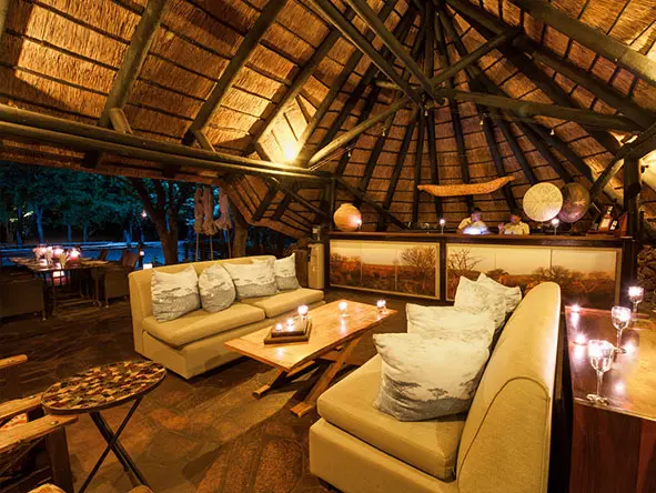El salón principal y el bar del lodge están bajo un techo de paja y dan a una terraza exterior con vistas a la charca.
