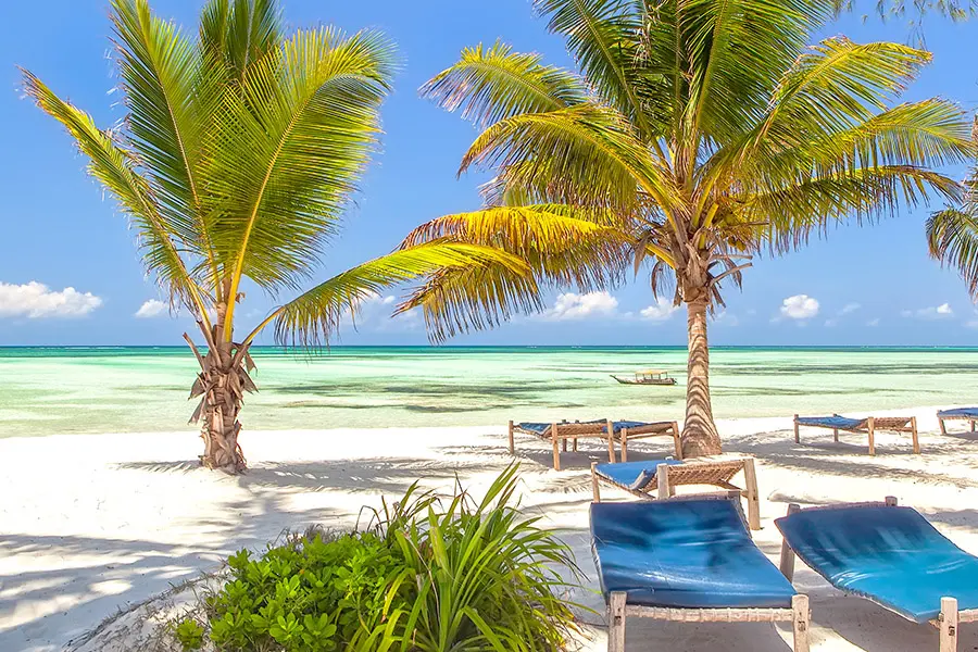 Tumbonas de playa bajo hojas de palmera a orillas del océano Índico, Zanzíbar, Tanzania