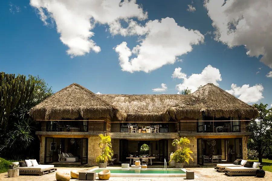 Looking across towards a double storey thatched building with a pool in front of it with a handful of surrounding loungers | Go2Africa