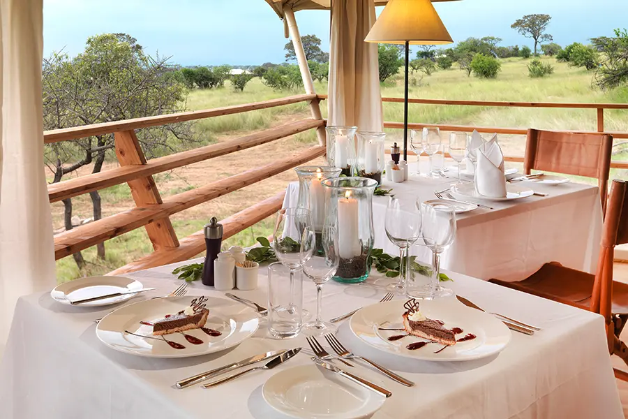 A beautifully set table for two features a slice of chocolate torte and wine glasses with two lit candles overlooking the surrounding Serengeti | Go2Africa