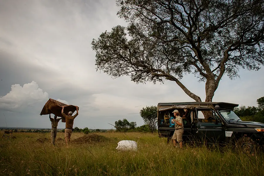 Un vehículo de caza de Serian the Original y dos hombres preparando una manta de picnic | Go2Africa