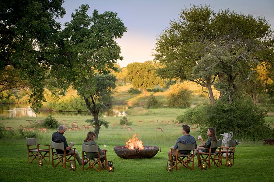 Varios huéspedes se reúnen en torno a la hoguera en Singita Castleton | Go2Africa