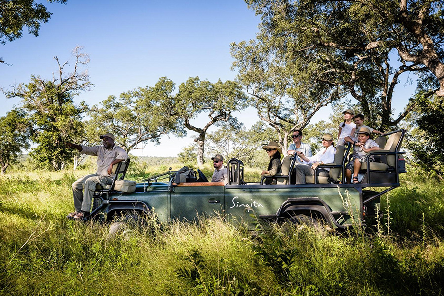 A group of people on a game vehicle look to the left as their guide points towards a sighting out of frame | Go2Africa
