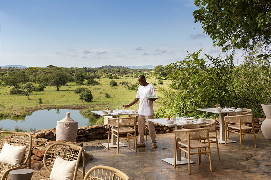 Wicker-style chairs and small tables sit on a raised deck overlooking a body of water and across part of the Grumeti Game Reserve | Go2Africa