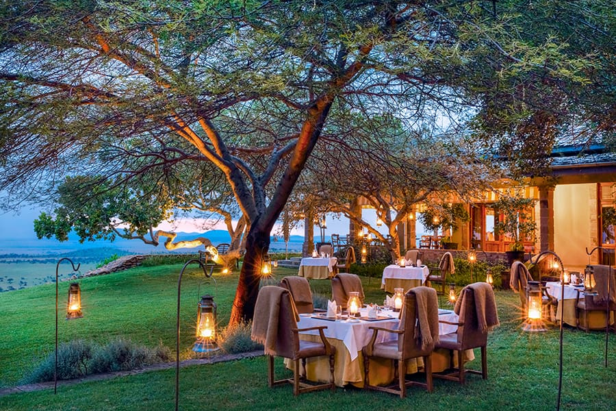 Mesas dispuestas bajo un árbol para la cena con farolillos alrededor en Singita Sasakwa | Go2Africa