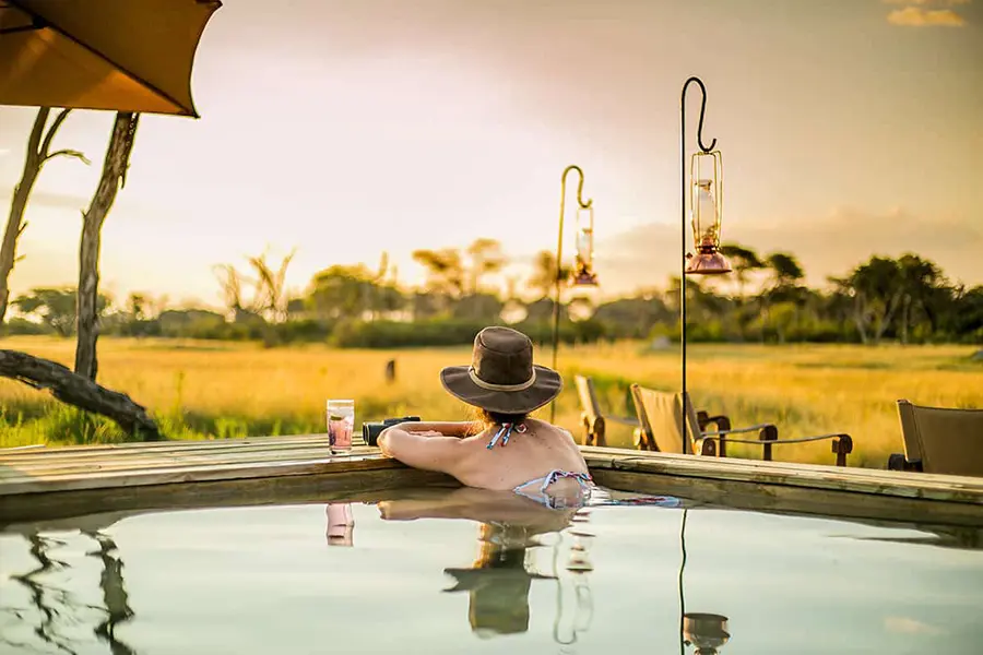 Una mujer con sombrero de ala ancha mira hacia otro lado mientras se sumerge en una piscina y contempla la selva circundante | Go2Africa