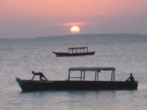 A pair of Zanzibari boats bob up & down in the gathering dusk while the sunset burns the sky.
