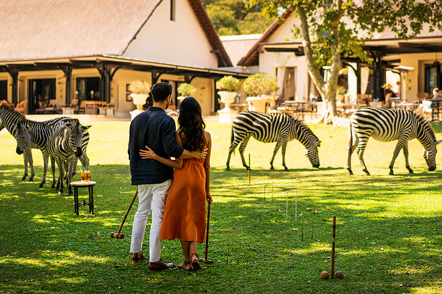 A couple playing lawn games admire several zebra grazing at The Royal Livingstone hotel | Go2Africa