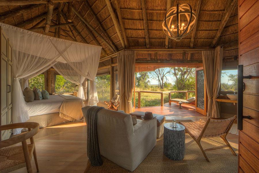 A luxurious interior with four-poster bed and balcony beyond look into the bush surrounding Camp Moremi | Go2Africa