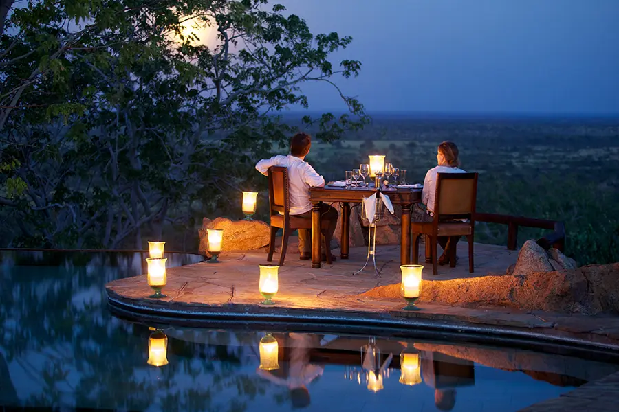 Two people overlook part of the Meru National Park from their hilltop position while having a candle- and lantern-lit dinner by the pool at Elsa's Koje in Kenya | Go2Africa