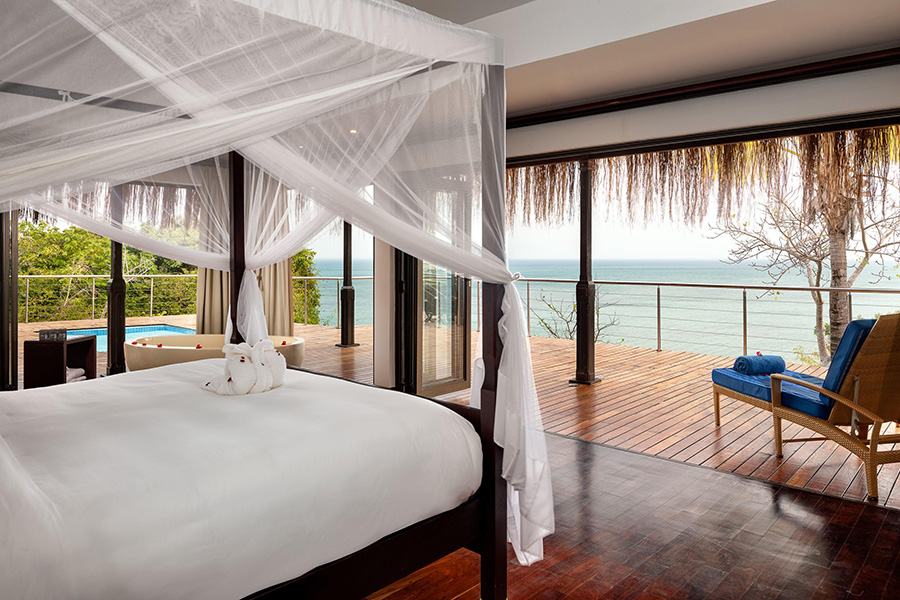 A four poster bed with mosquito net facing an ocean view with a plunge pool on a surrounding deck | Go2Africa