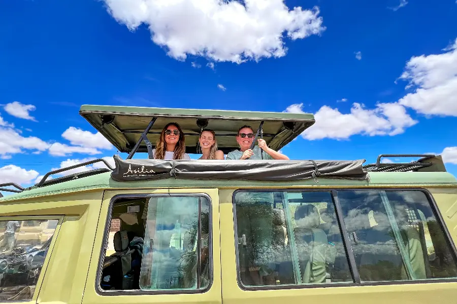 3 mujeres salen por la parte superior de un vehículo de caza Asilia con el cielo azul de fondo | Go2Africa