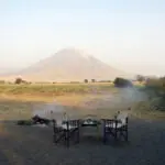 Comparta historias de safari alrededor de la hoguera bajo la atenta mirada del volcán Oldoinyo Lengai.