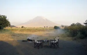 Comparta historias de safari alrededor de la hoguera bajo la atenta mirada del volcán Oldoinyo Lengai.