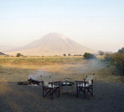Share safari stories around the campfire under the watchful eye of Oldoinyo Lengai volcano.