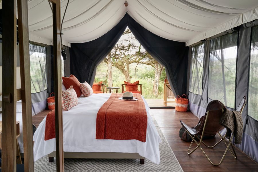 A large bed in a spacious tent with small balcony complete with safari-style chairs and views across to trees and wildlife | Go2Africa