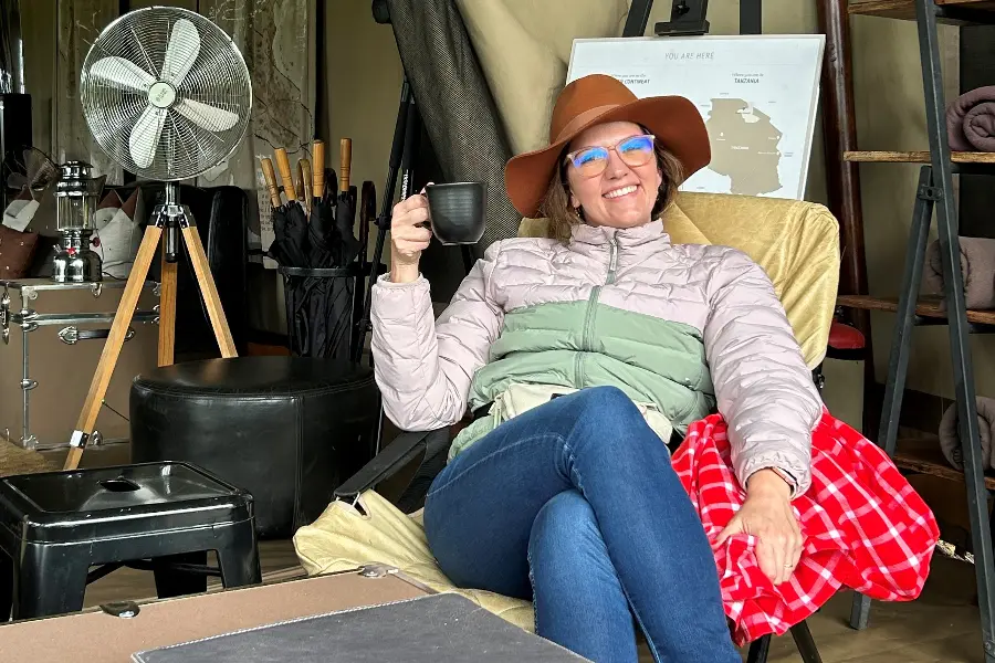 Una mujer sentada en una silla de camping con una bebida caliente y una manta | Go2Africa