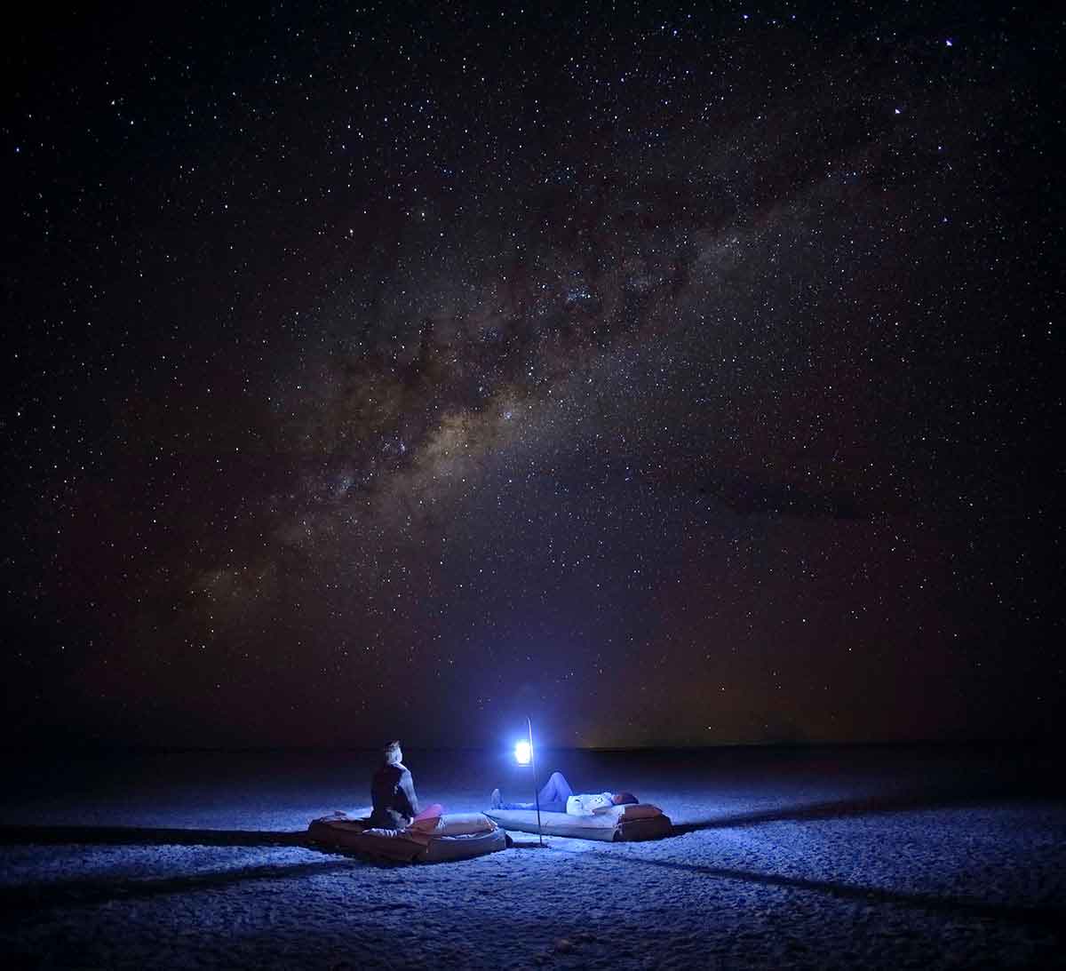 Two guests sit around a lamp, enjoying a sleep-out at Meno-a-Kwena in the Kalahari, Botswana