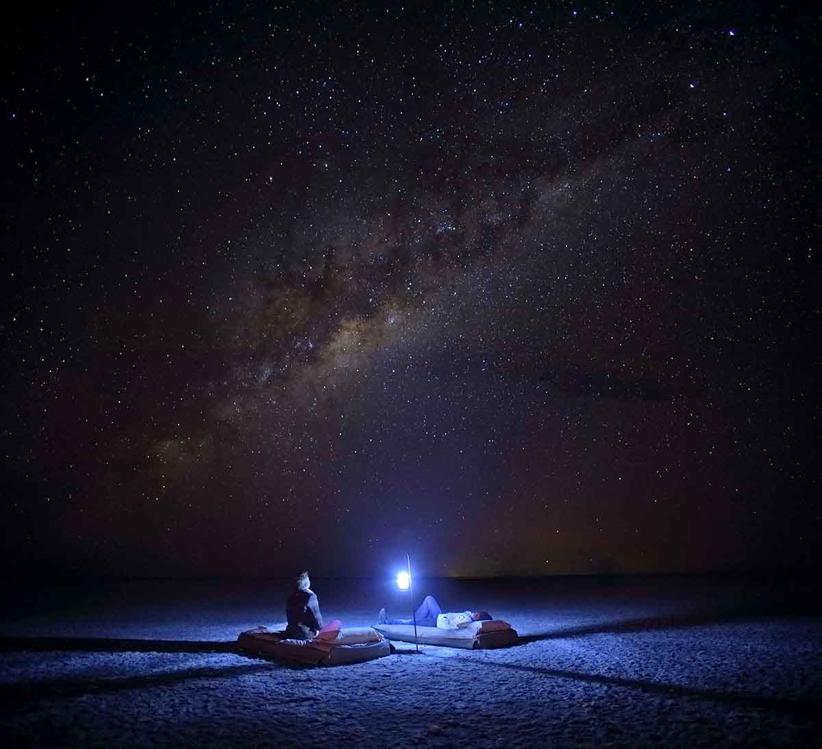 Dos huéspedes sentados alrededor de una lámpara, disfrutando de un sueño en Meno-a-Kwena en el Kalahari, Botsuana.