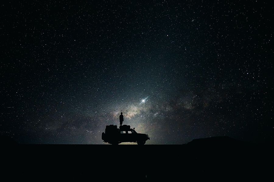 Person stands on top a game drive vehicle in the night sky of Namibia.