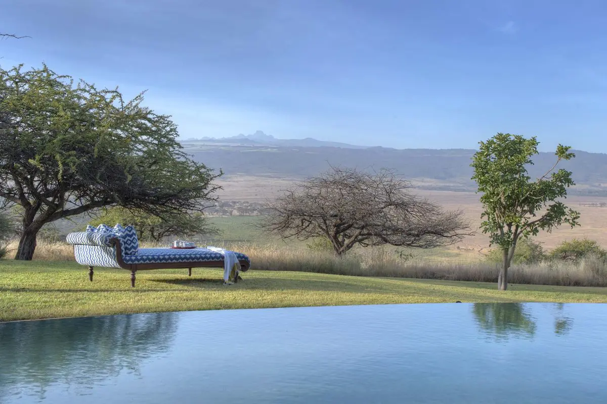 A blue and white chaise lounge sits by a body of water with a few trees dotted around looking at a view | Go2Africa