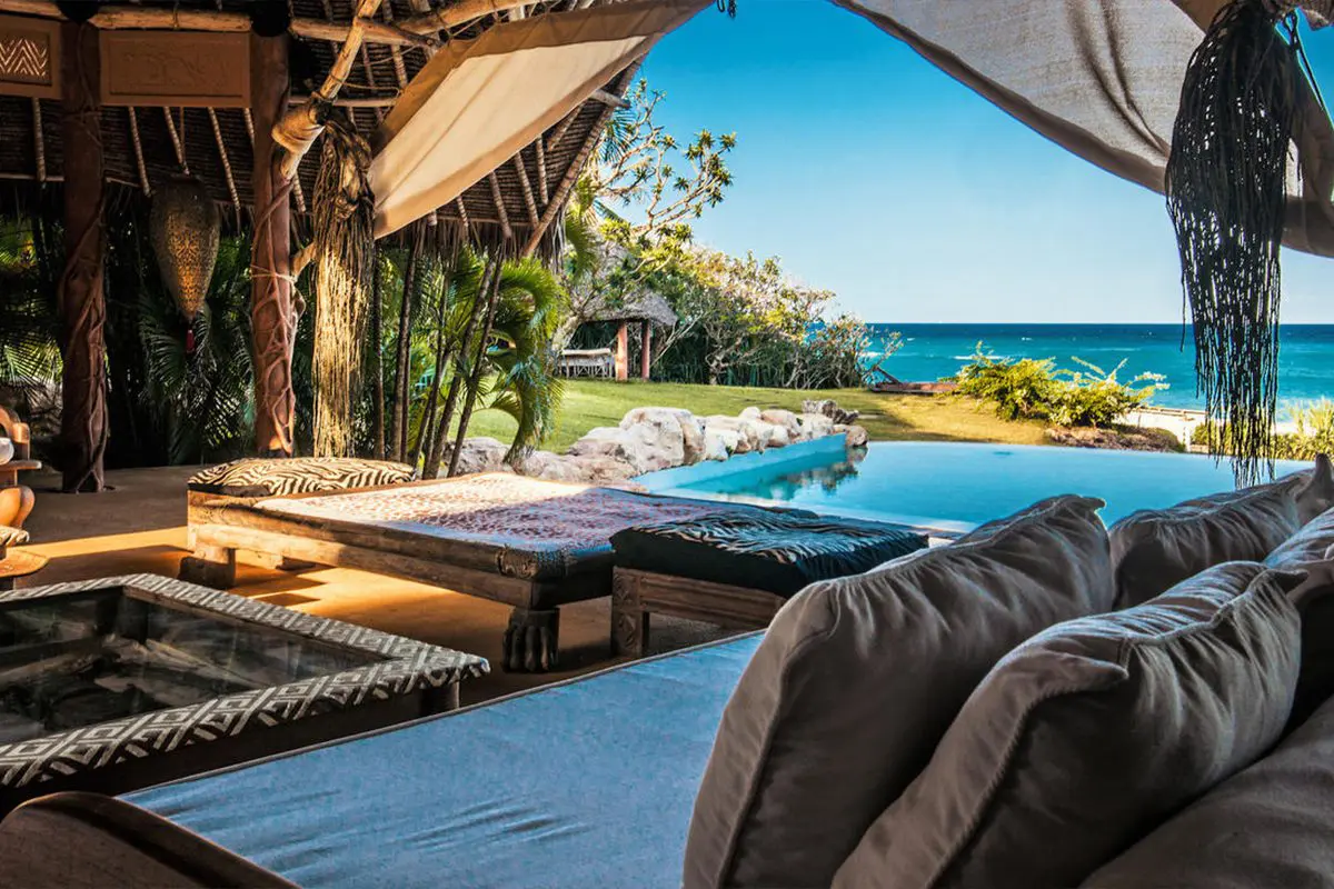 A view from the side of a semi-enclosed seating area with a swimming pool at the edge of it overlooking the beach and ocean | Go2Africa