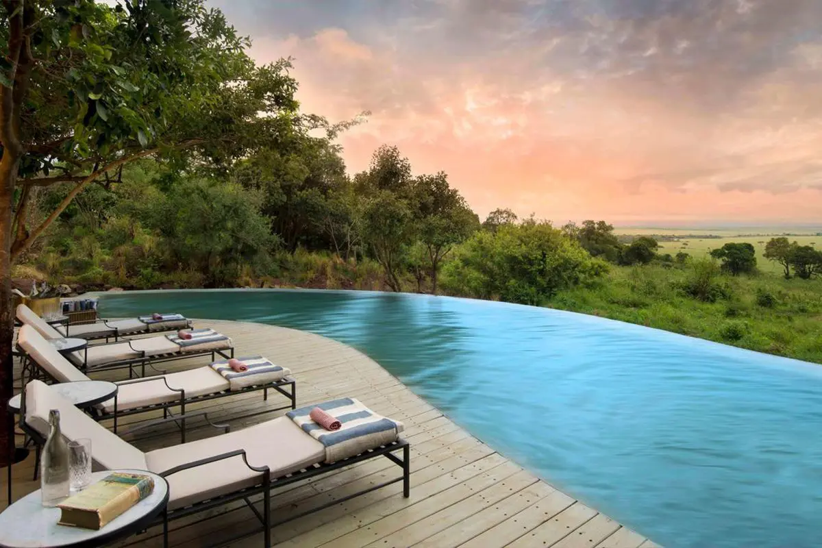 A curved pool and deck with four pool loungers look out over lush green grass and trees with a candyfloss sky | Go2Africa