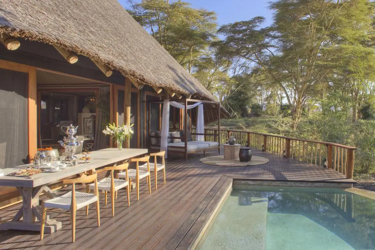 A large wooden deck complete with pool features a spacious table set up with some breakfast next to a thatched building | Go2Africa
