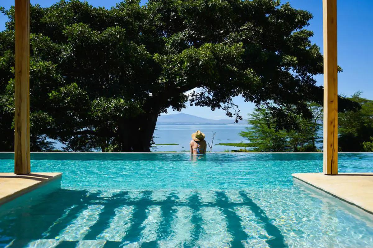 A woman in waist high water in the pool faces away from the camera looking over a body of water beyond | Go2Africa