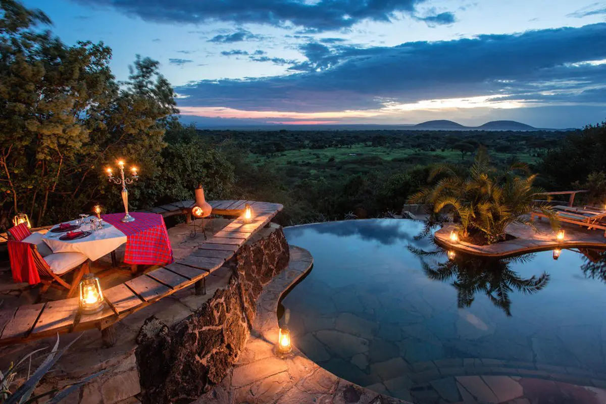 A small table set up for a romantic dinner for two is next to a pool overlooking the surrounding bush from its elevated position in Kenya | Go2Africa