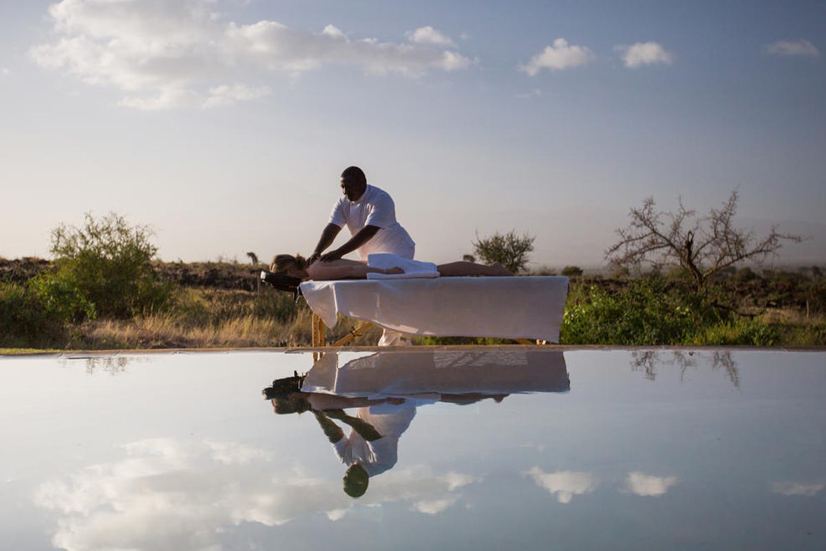 A pristine pool reflects someone receive a massage on a treatment table and the spattering of clouds in the sky, but not the greenery found behind the people | Go2Africa
