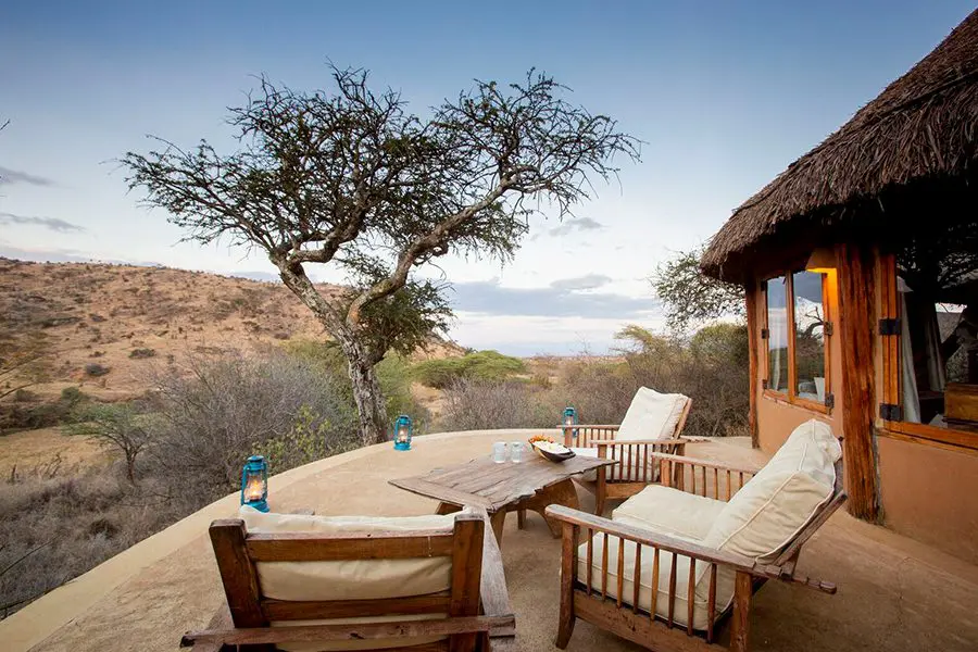 A deck with 3 spacious, cushioned chairs, a small table, and several lanterns sits outside a suite at Lewa Wilderness Lodge | Go2Africa