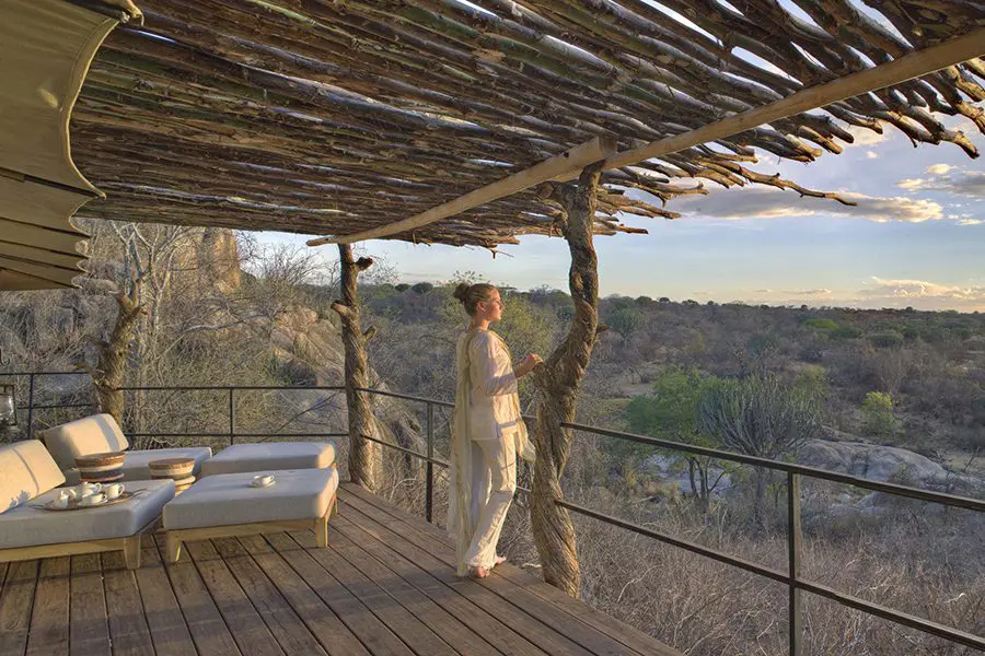 A woman stands at the edge of a wooden balcony overlooking vast views of the Serengeti from Mwiba Lodge | Go2Africa