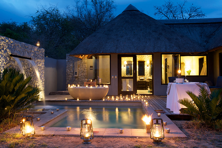 A private plunge pool with fountain feature is surrounded by lanterns and candles with an outside bathtub and table set up for a romantic dinner | Go2Africa