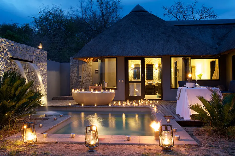 A private plunge pool with fountain feature is surrounded by lanterns and candles with an outside bathtub and table set up for a romantic dinner | Go2Africa