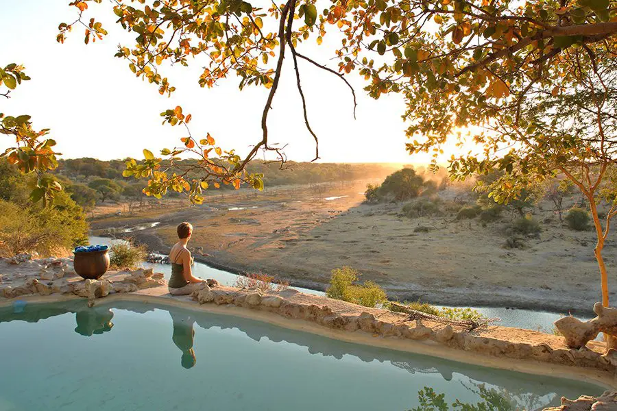 Una señora sentada al borde de una gran piscina con vistas a un río y más allá a la vida salvaje | Go2Africa