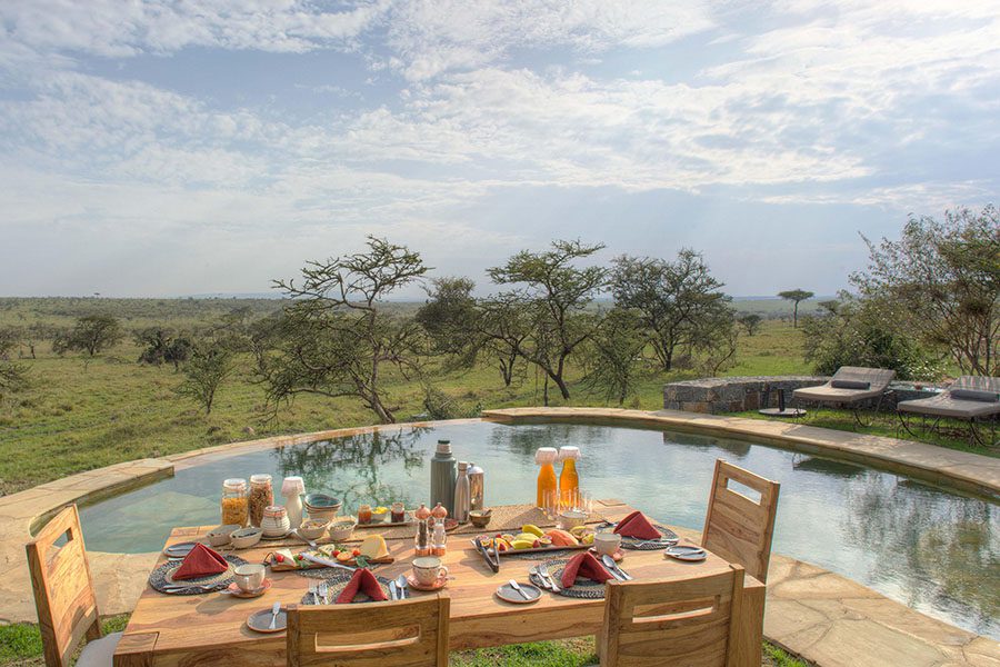 A wooden dining table with a breakfast spread set up by the pool at Naboisho Camp | Go2Africa